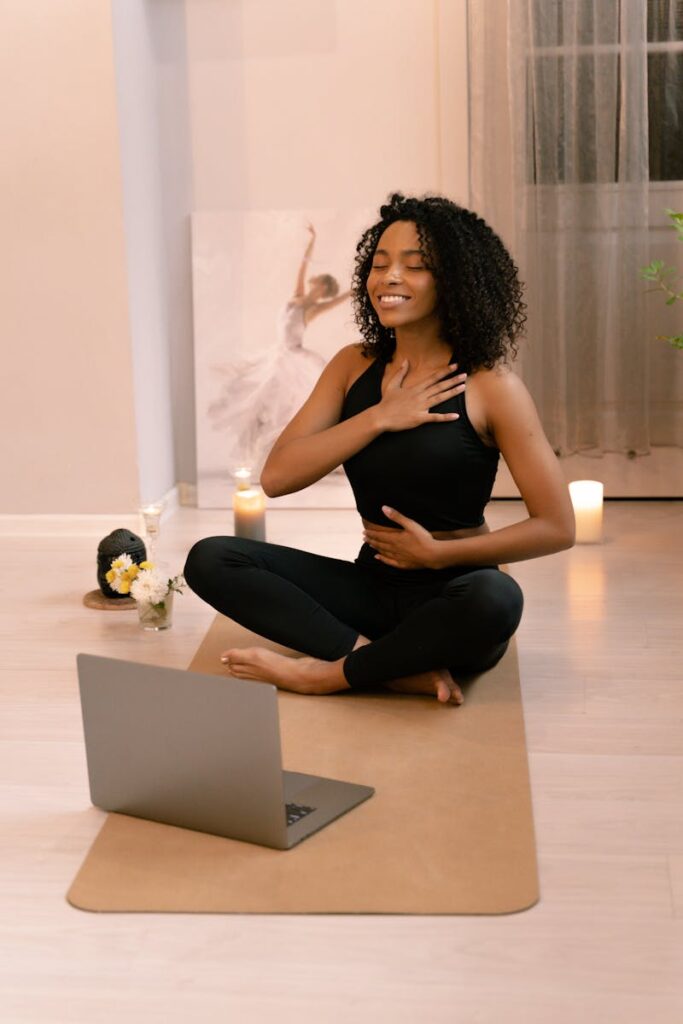 African American woman practicing yoga and meditation indoors with a laptop.