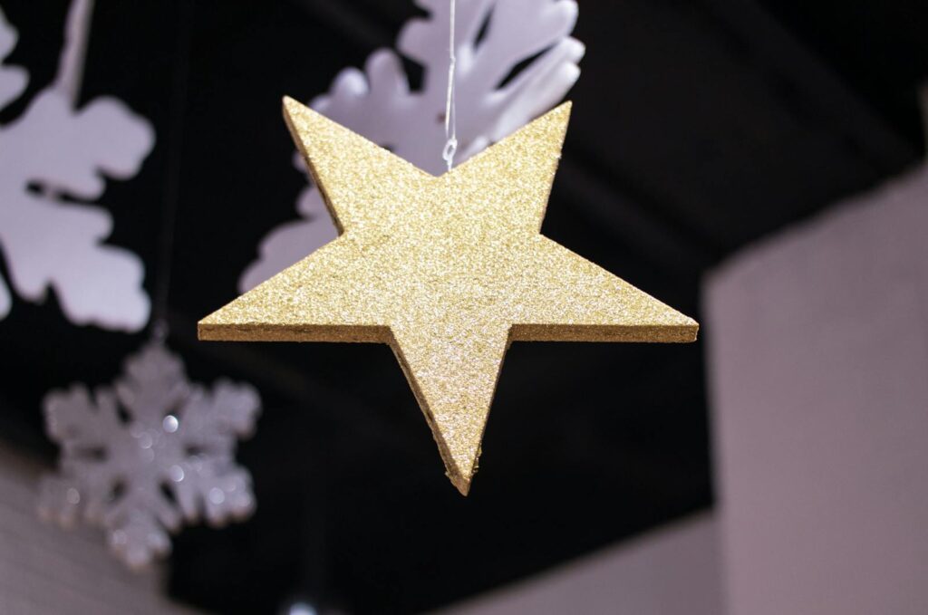 A glittering gold star decoration hanging among white snowflakes for festive decor.