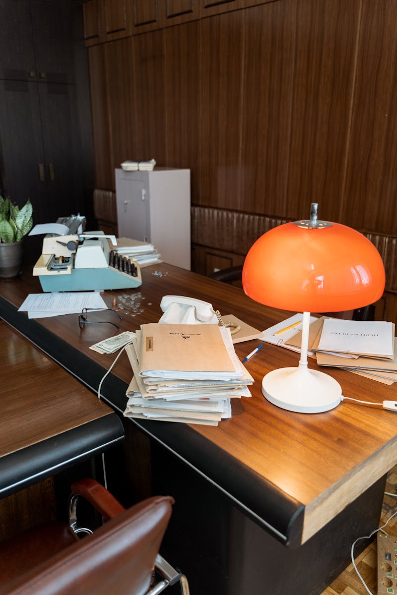 A classic workspace with a retro lamp, typewriter, and stacked papers, evoking 80s and 90s nostalgia.
