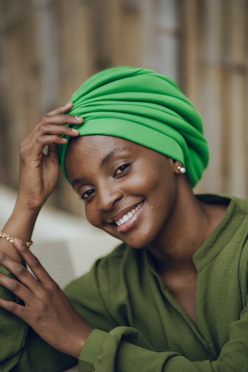 Elegant portrait of a smiling woman wearing a green headwrap and earrings in Nigeria.